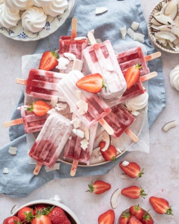 Ice lollies on a plate with strawberry, coconuts and meringues
