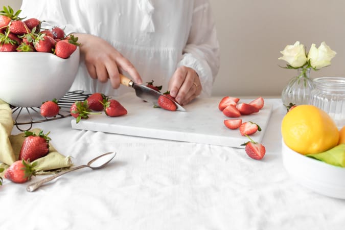 Woman cutting Strawberry with a knife on marble chopping board