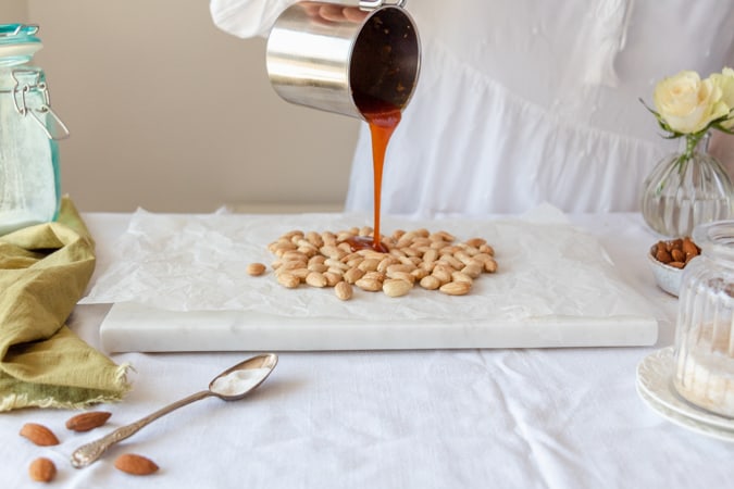 Woman poring caramel over roasted almond on marble chopping board
