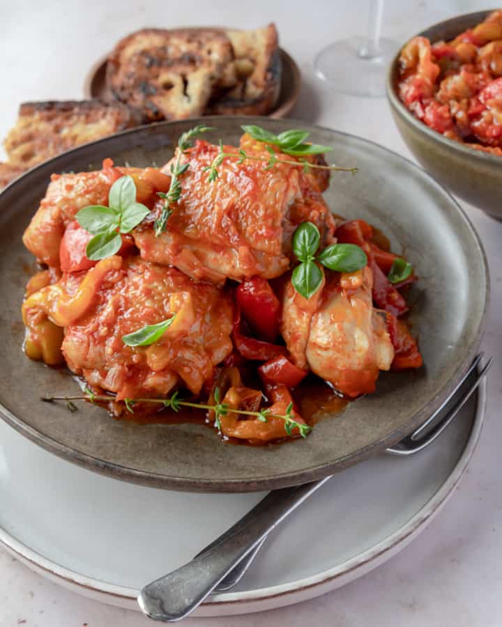 One-pot Italian chicken with peppers and onion sauce with tomatoes on a brown plate with some slices of toasted bread 