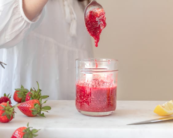 woman dropping strawberry jam with a spoon on jar