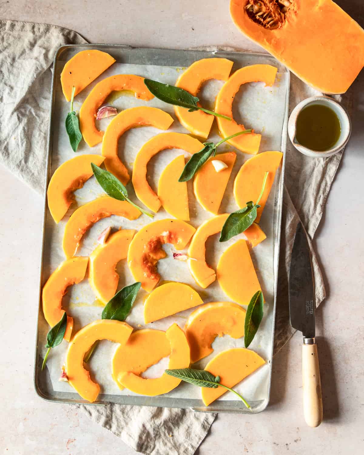 slices of butternit squash on a tray with sage and olive oil