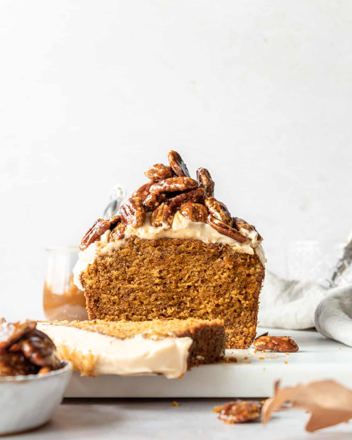 Pumpkin cake with a slice of cake on a marble tray with a bowl full of caramelized pecans