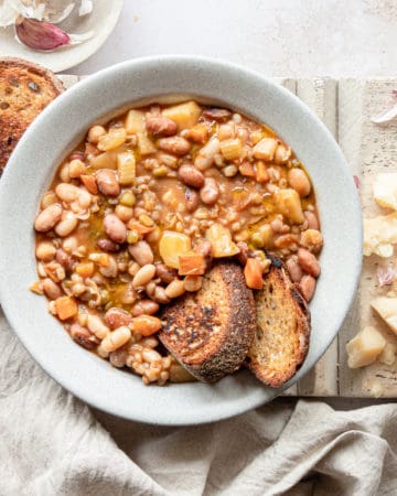 Beans soup on a bowl with two slices of bread on it next some pieces of Parmgiano Reggiano