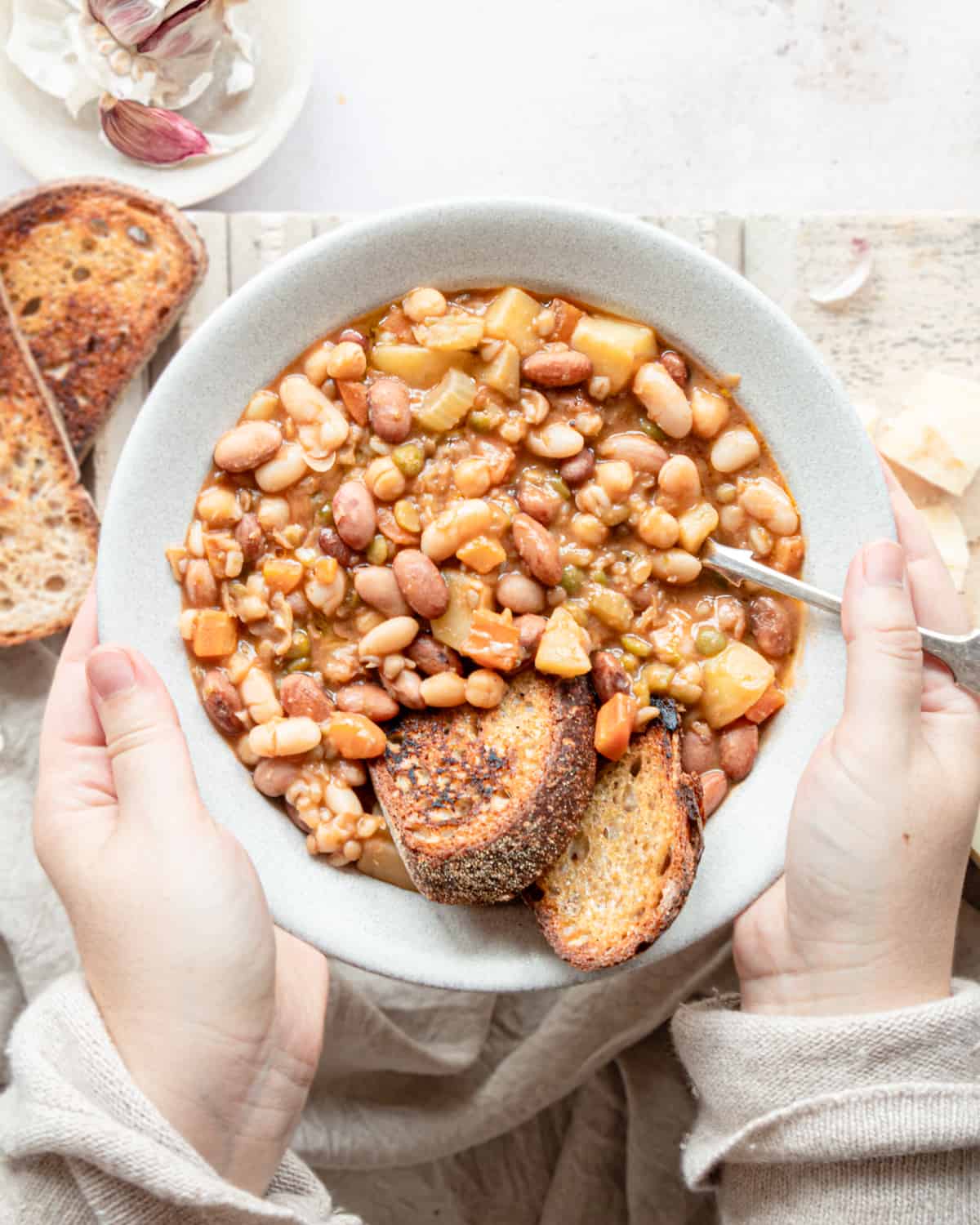 Beans soup in a bowl with 2 slices of bread  and a spoon on it, hold it by two hands. 