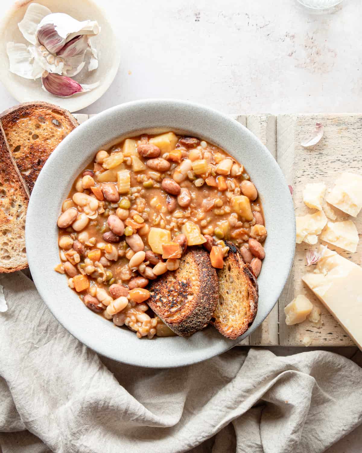 Beans soup in a bowl with 2 slices of bread next to some pieces of Parmigiano Reggiano.