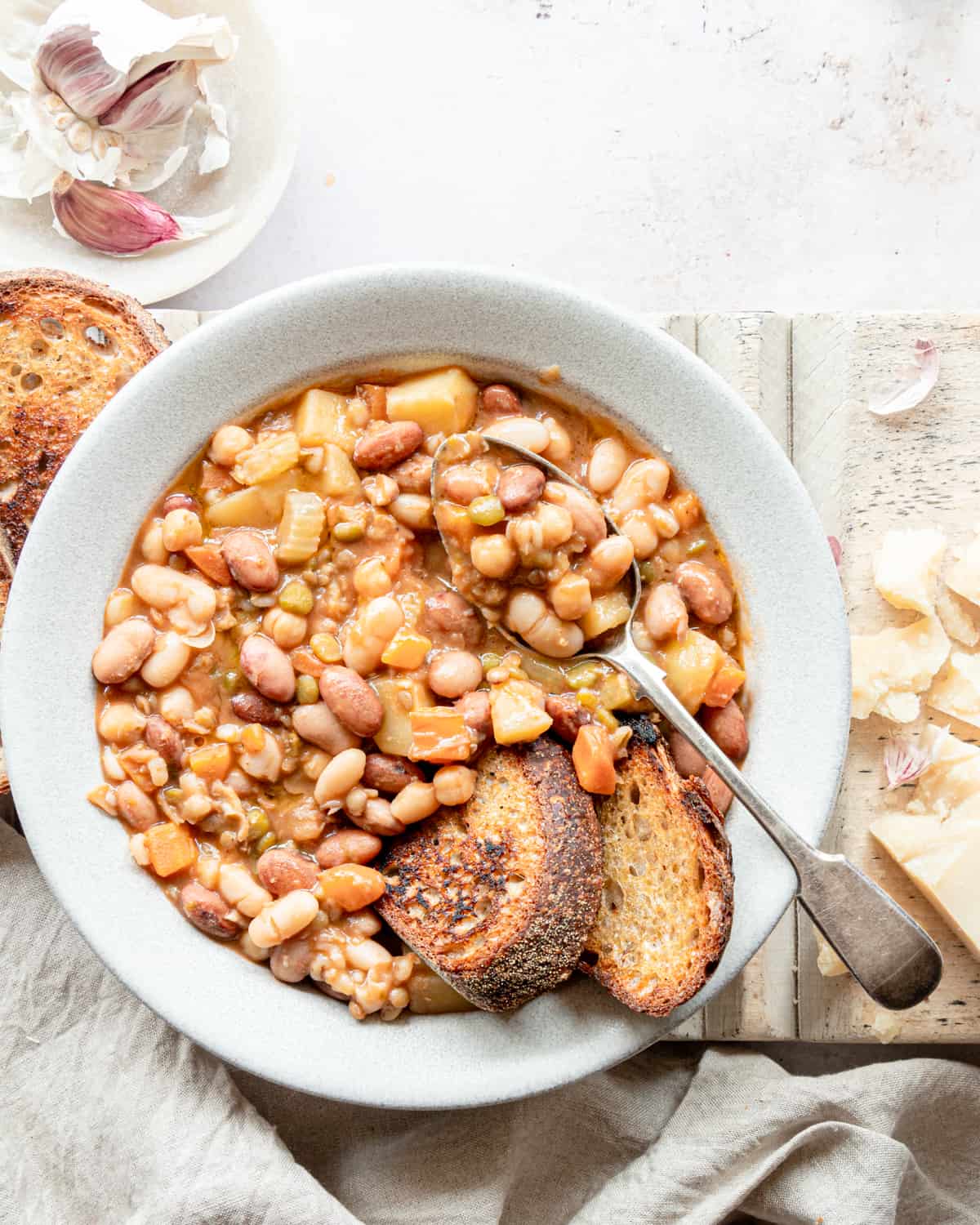 Beans soup in a bowl with 2 slices of bread  and a spoon on it next to some pieces of Parmigiano Reggiano