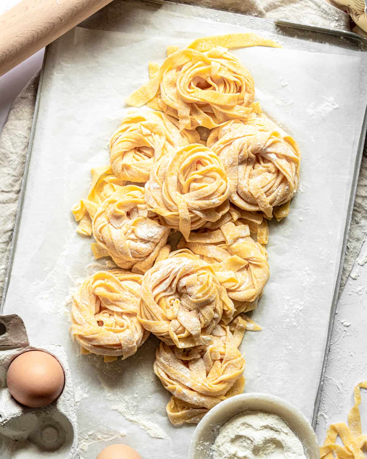 Nest of homemade pasta on a tray with eggs and a rolling pin