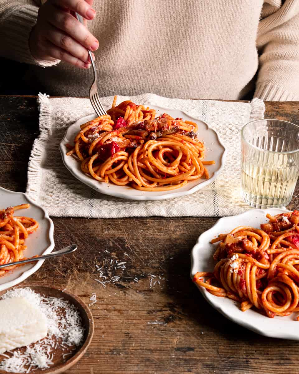 Pasta with amatriciana sauce on plates with a hand holding a fork