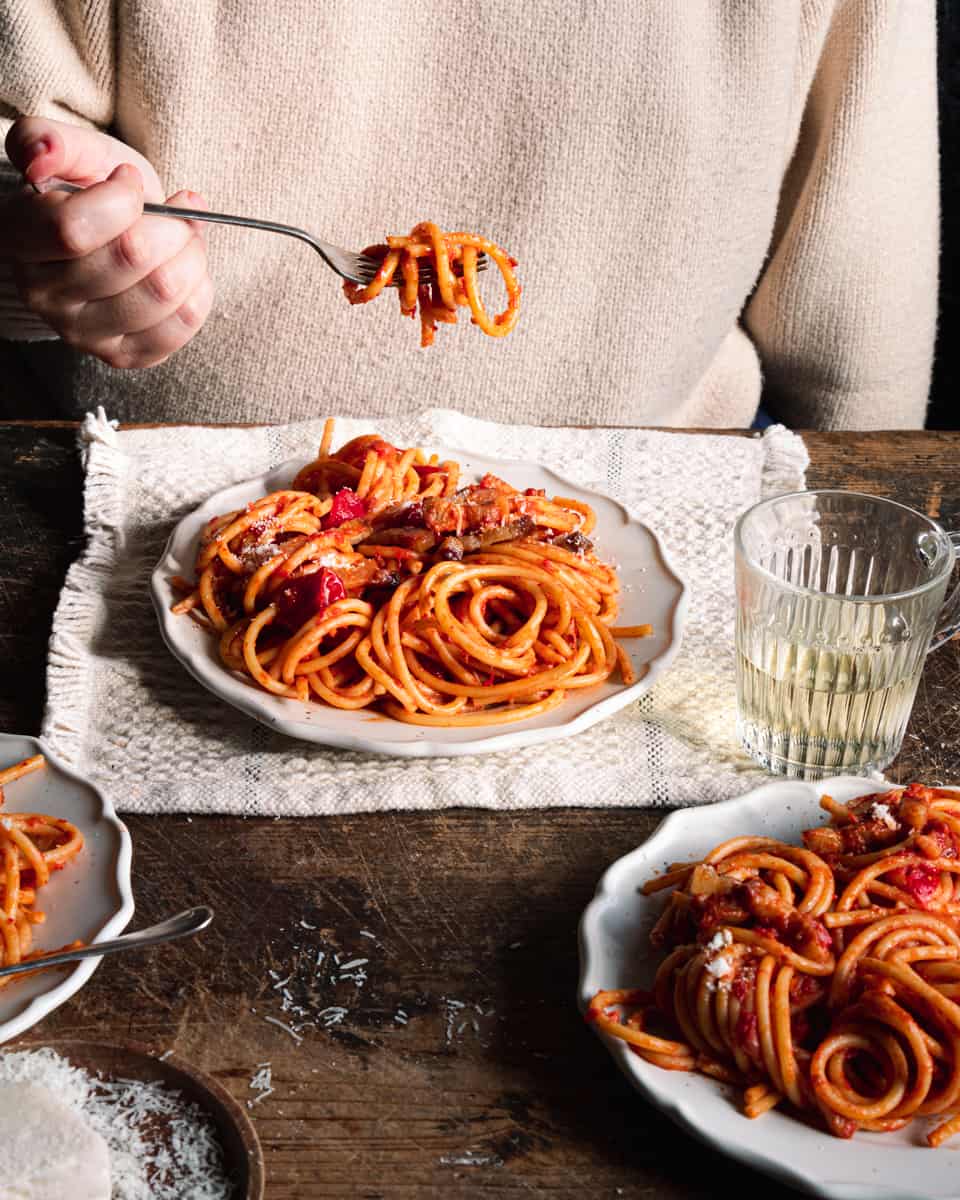 hands holding a fork with pasta and amatriciana sauce