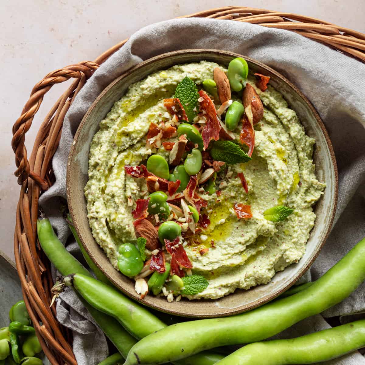 Broad beans pesto in a bowl placed in a wooden basket