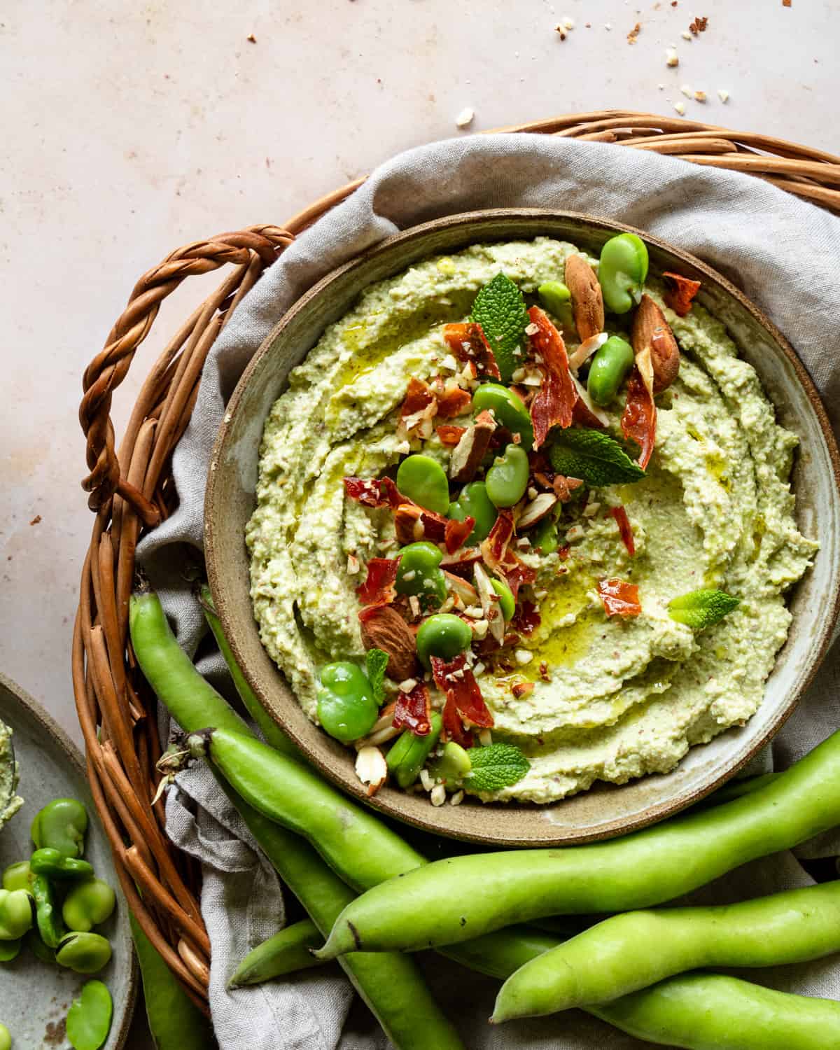  hummus  on a bowl, placed in a basket with broad beans. 