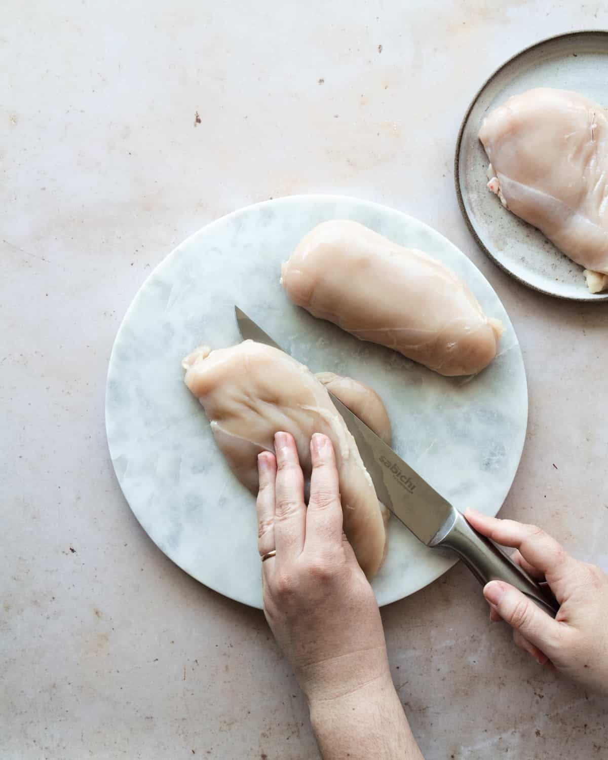 Hand slicing the chicken breast with a knife on a surface. 