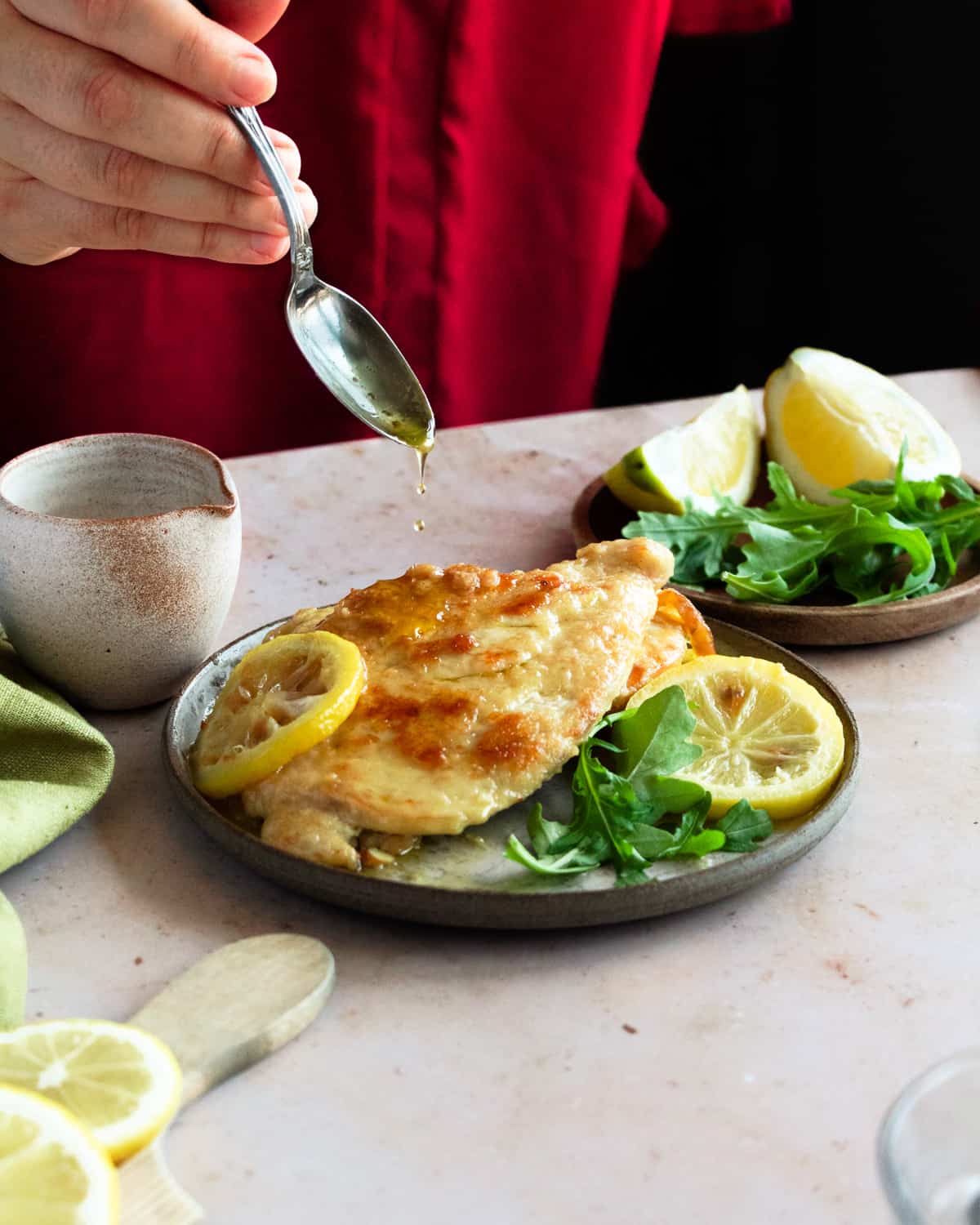 Hands dropping the sauce over the Chicken piccata al limone recipe.
