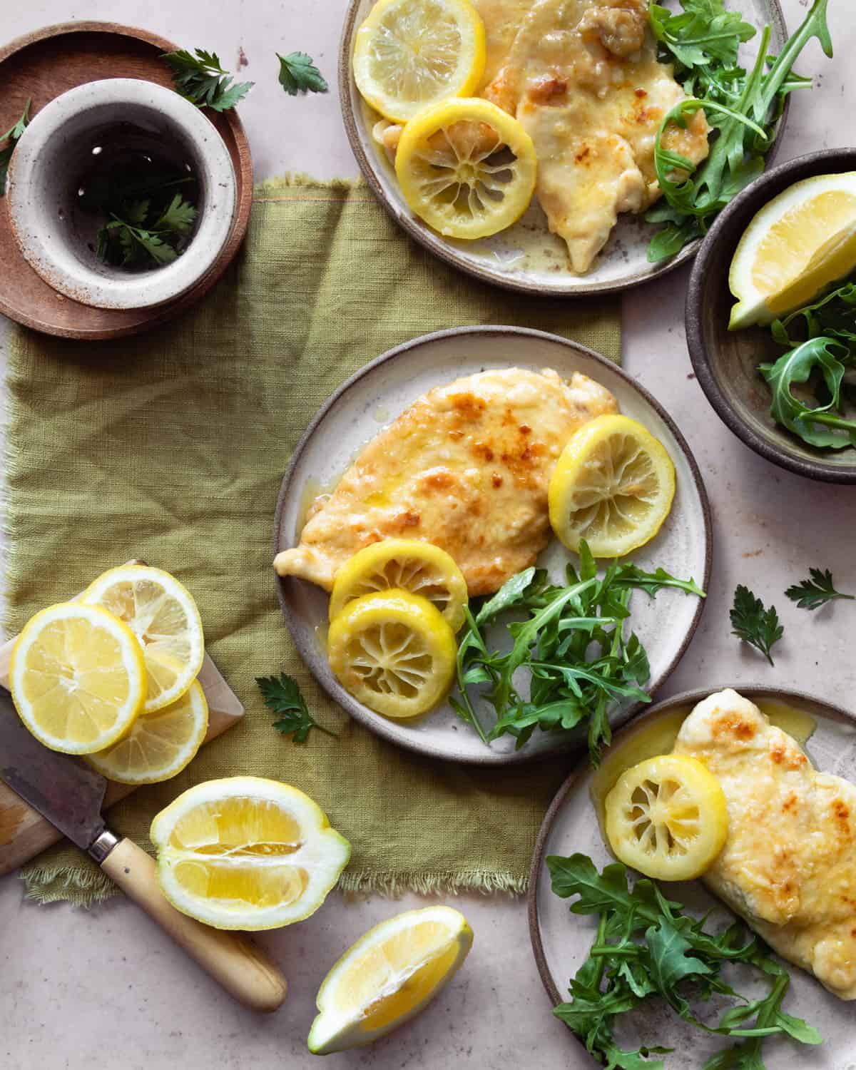 Chickens piccata al  limone recipe on plates with arugula and lemons slices around.