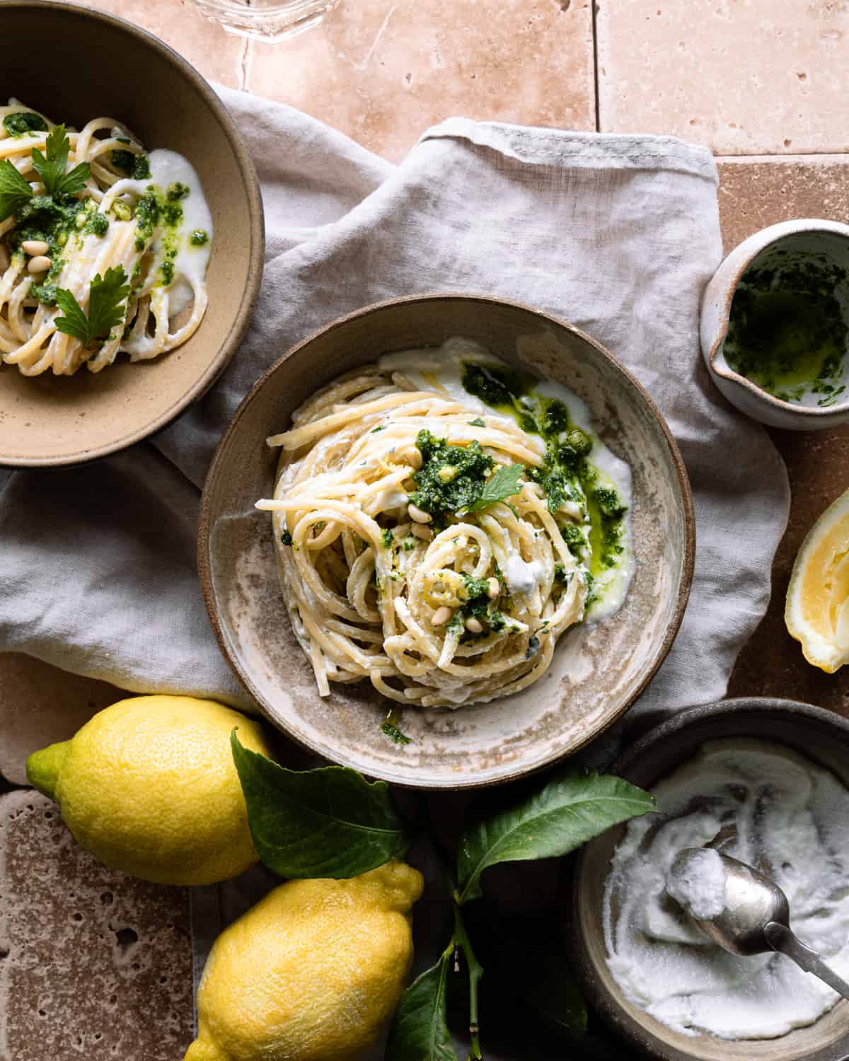 Pasta with ricotta and parsley pesto on two bowls on a kitchen towels near two lemons.  