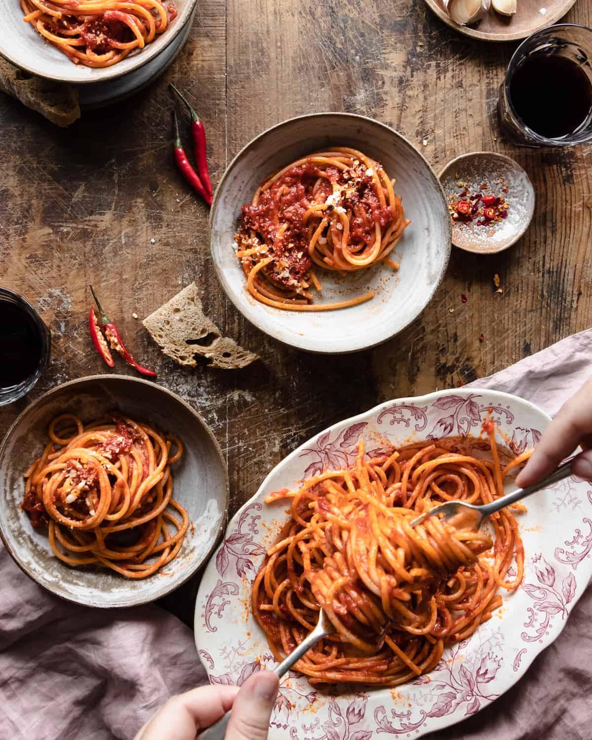 Spaghetti arrabiata on bowls on a wooden table with red chili peppers on top