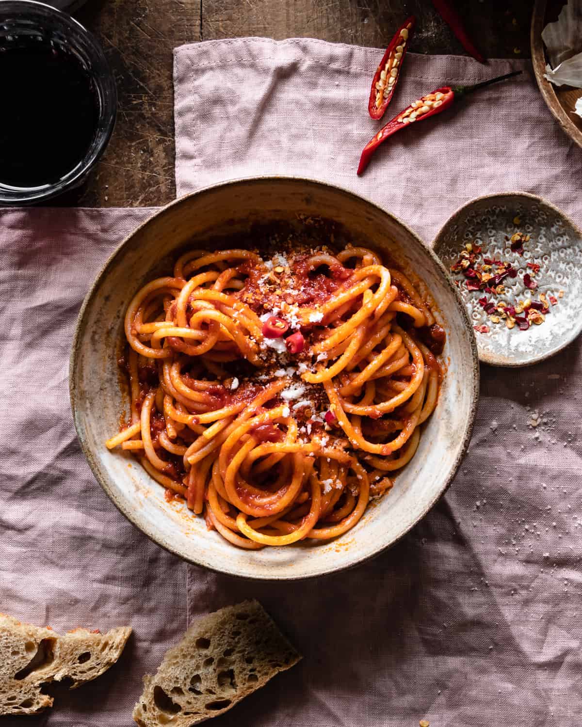 Spaghetti arrabiata on a bowl on a pink napkin with bread slices and red chili peppers around. 