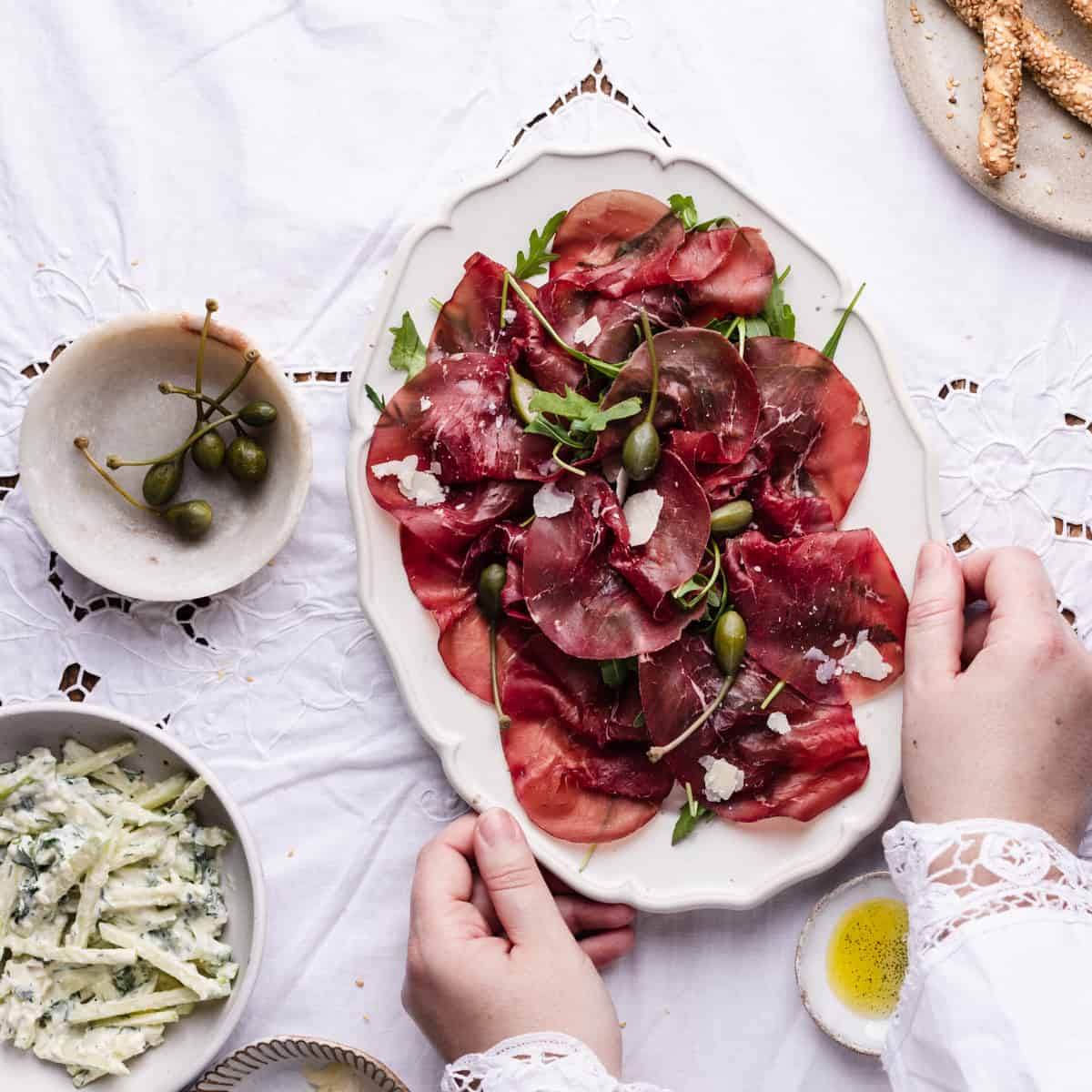 Bresaola di carpaccio in a serving dish with hand holding it