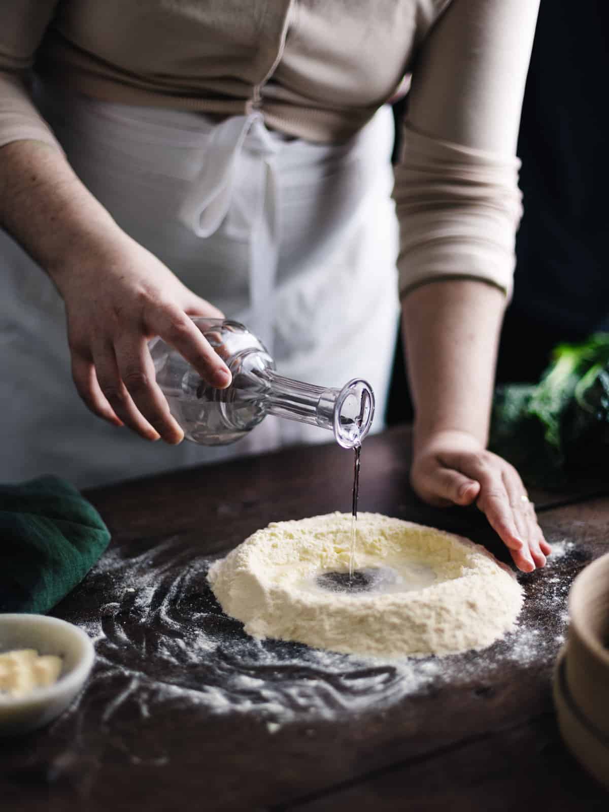 Side shot of woman pouring water inside the flour well to make gnochetti