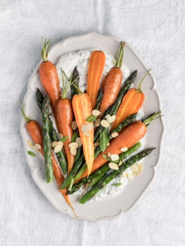 Overhead shot of serving plate with carrots and asparagus on a white table.
