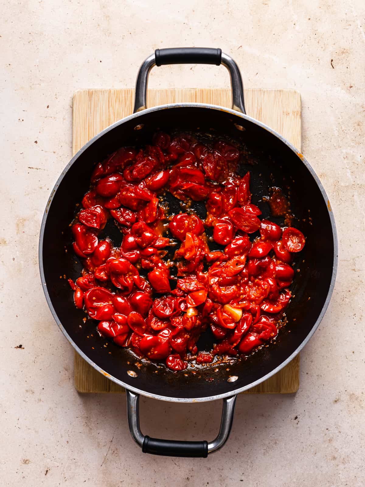 Overhead shot of a frying pan with cooked and squashed tomatoes.