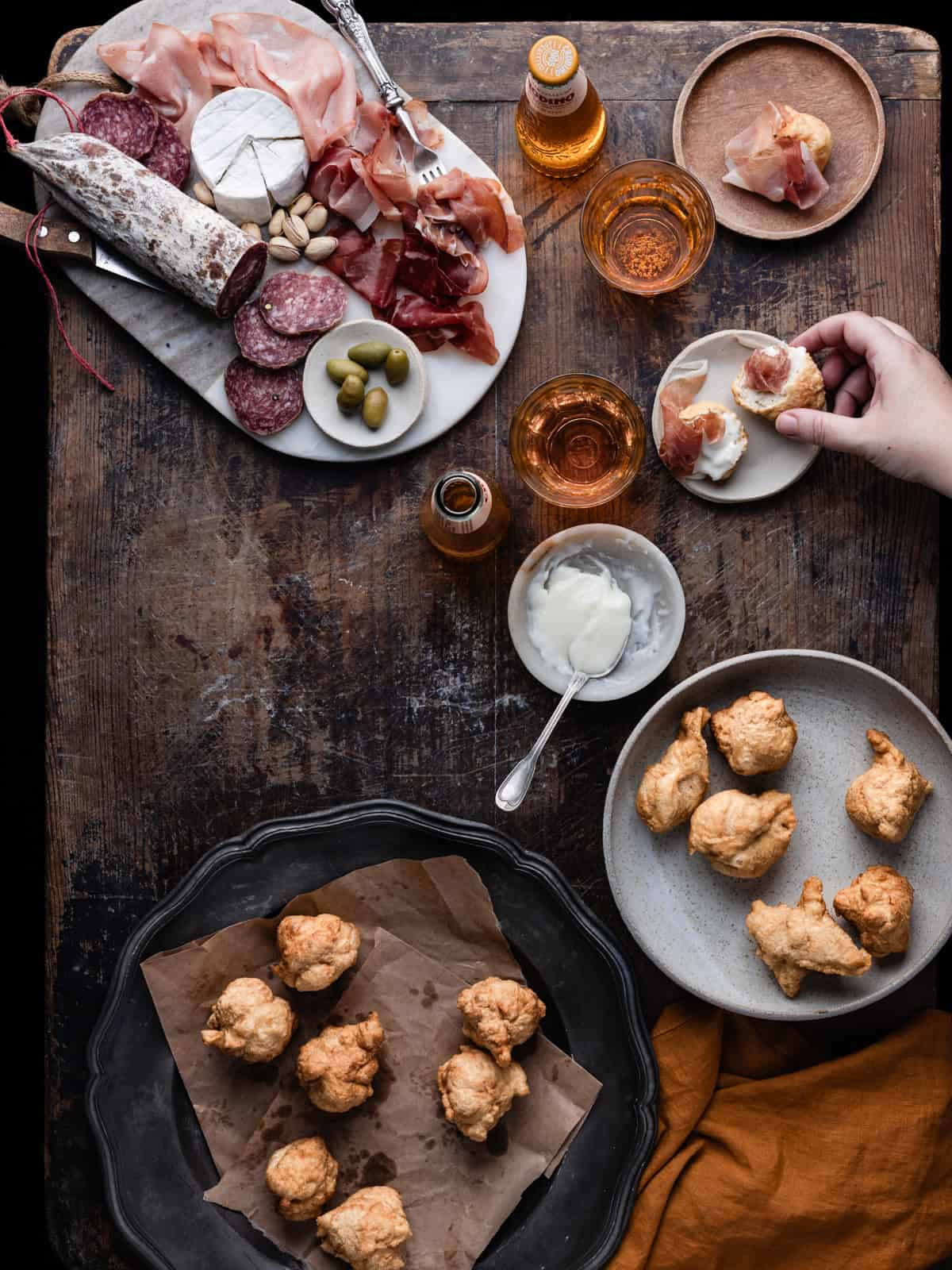 Fried coccoli on serving plate served on a table along with cheese and cured meats with hand reaching one fried bread ball stuffed with cheese and cured meat.