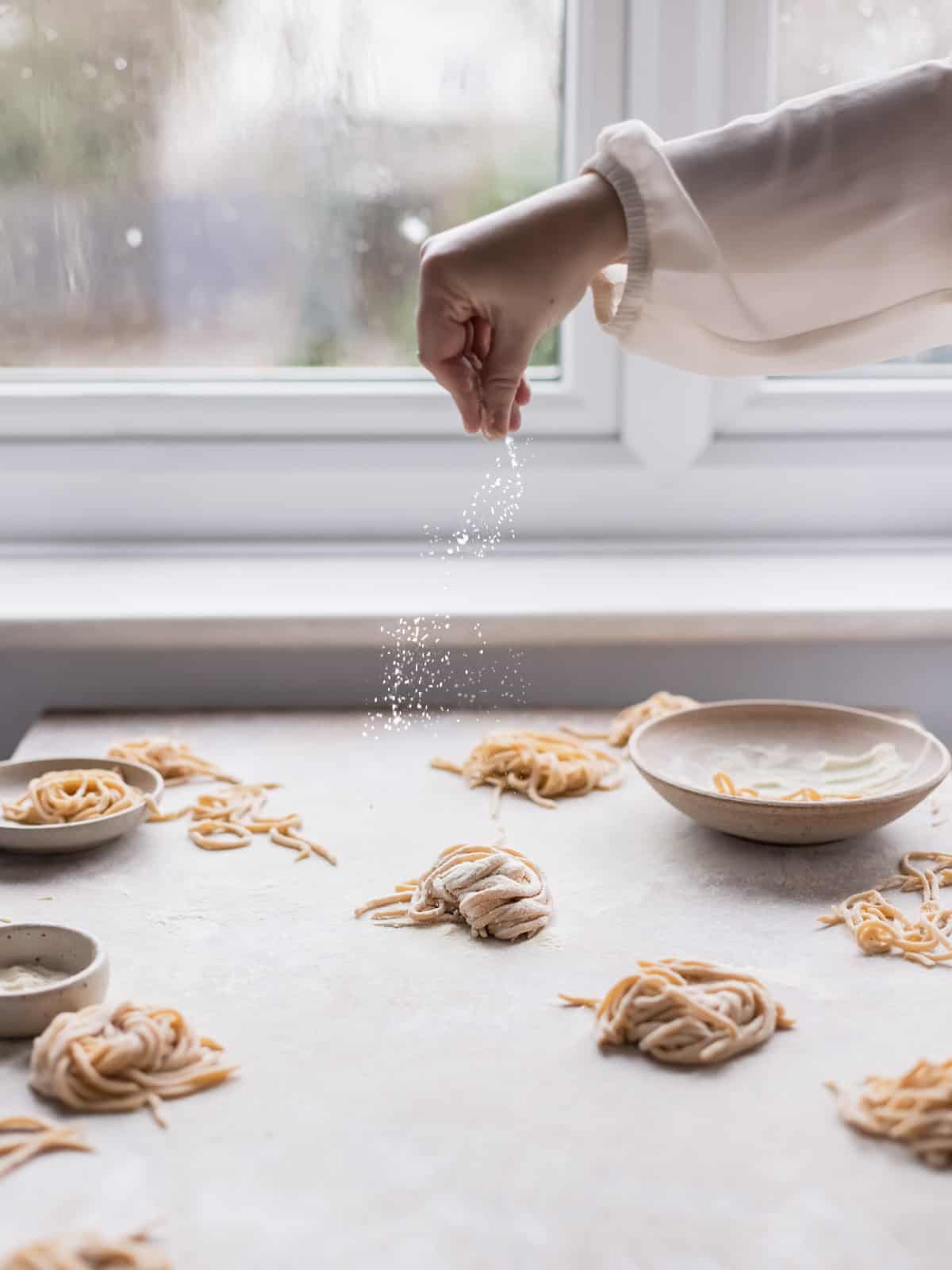 Hand dropping some flour on a pasta nest