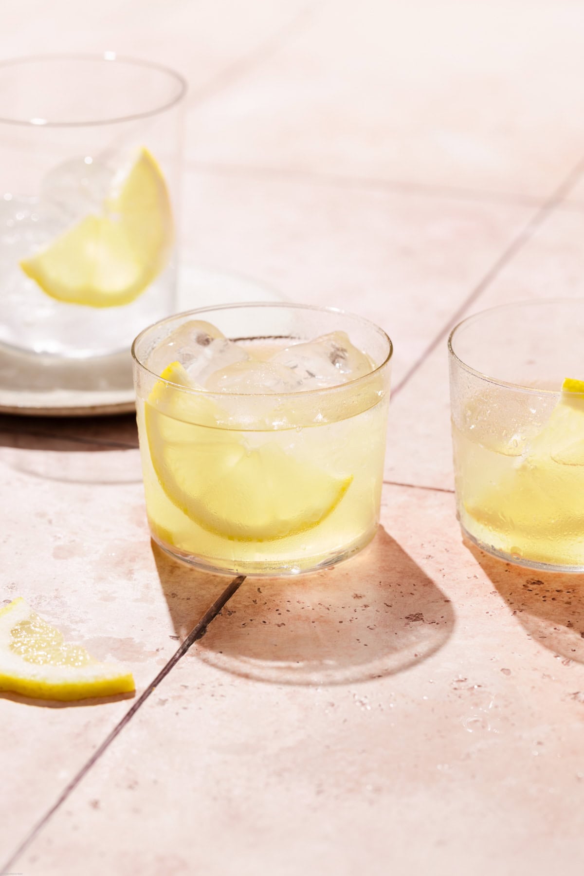 3 glasses filled with the Amalfi spritz limoncello and a slice of lemon on a pink backdrop.