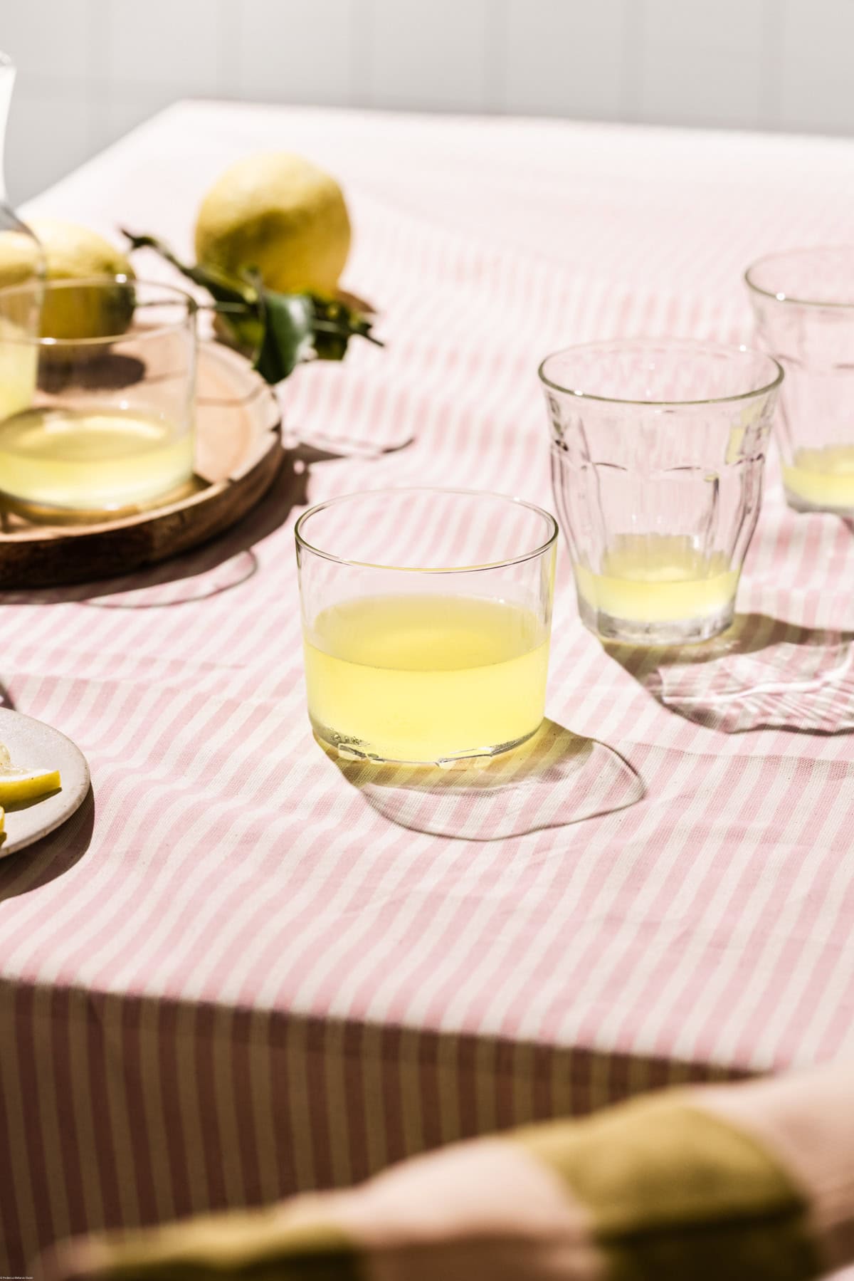 Glasses full of limoncello on a pink stripe tablecloth.