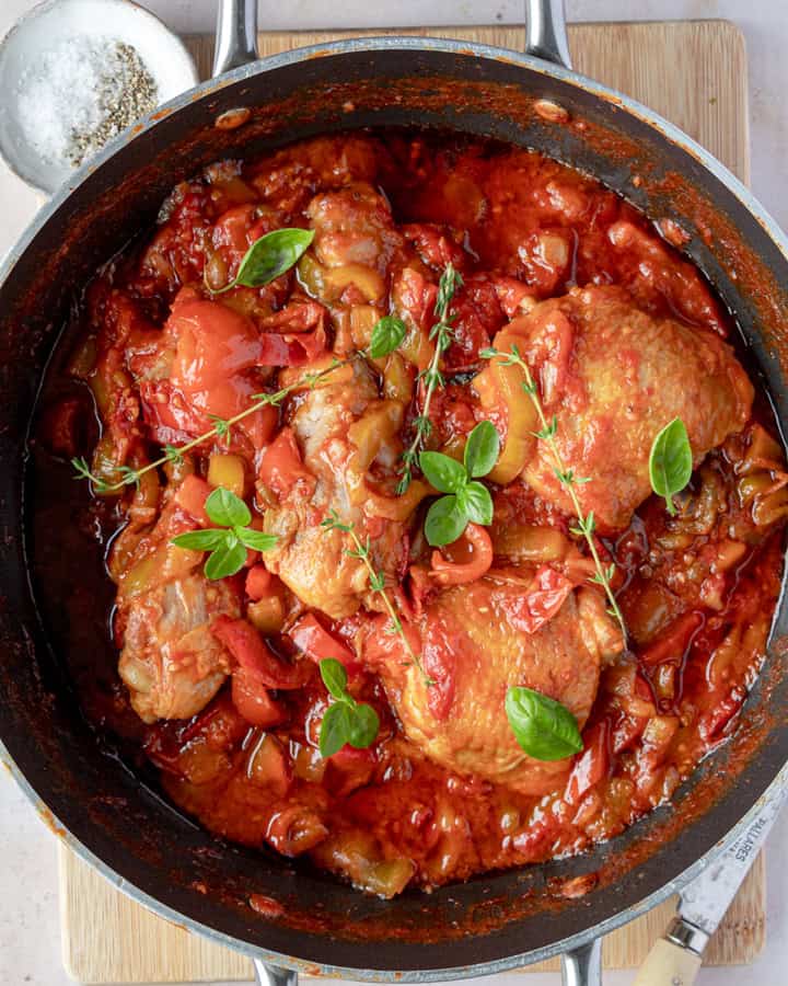 A close up of the chicken with tomatoes and peppers sauce on a pan topped with fresh herbs.