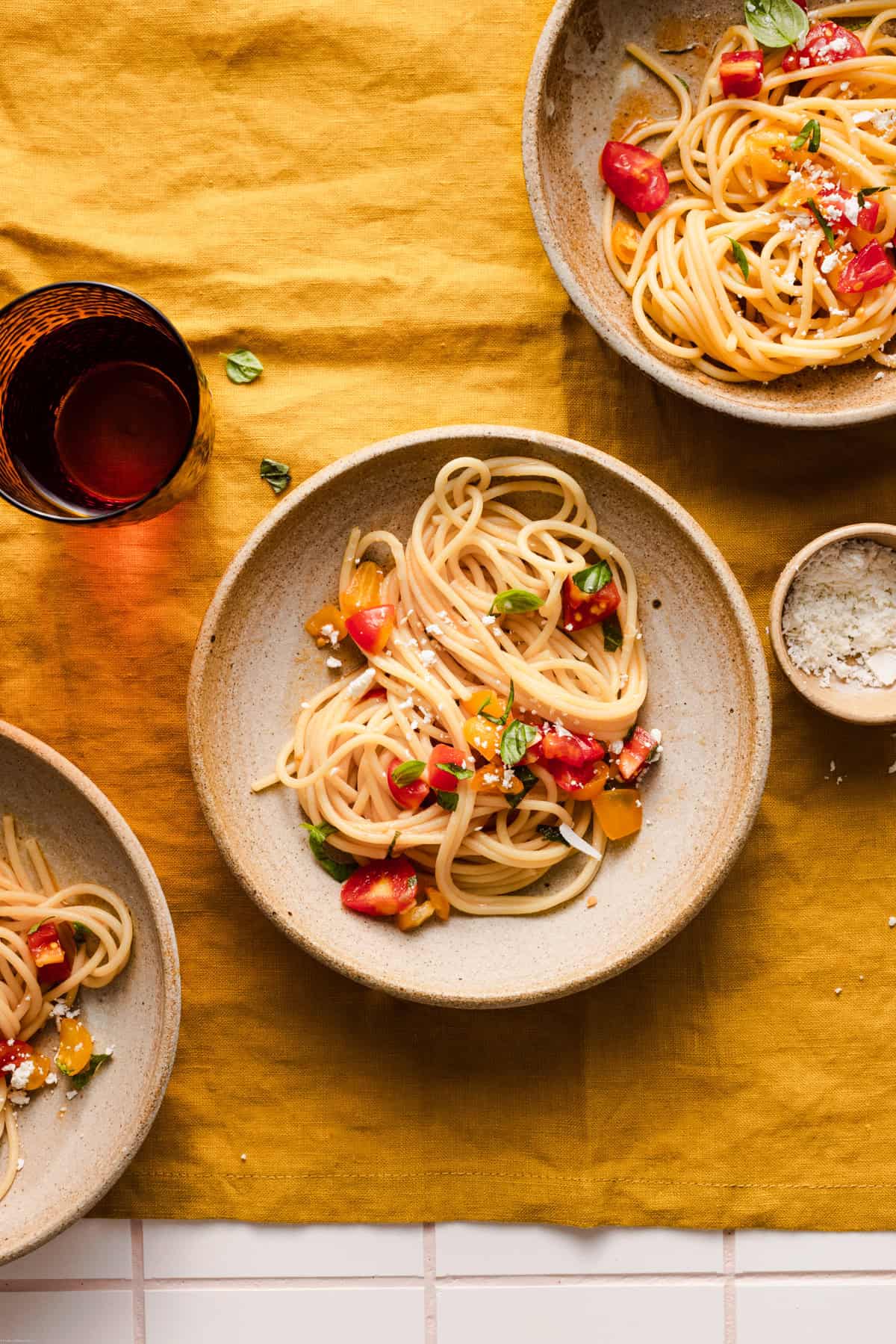 Spaghetti pasta crudaiola placed on different bowls on an orange linen with a water glass and pinch bowl around it.