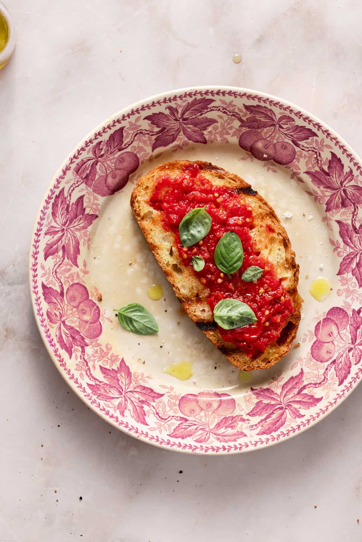 A slice of tomato and bread on a pink plate on a marble table.