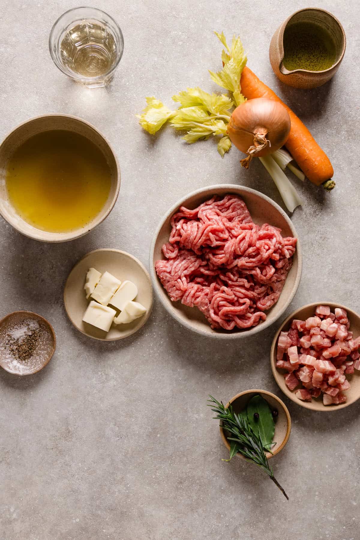 Ingredients to make the ragu on different bowls on a beige backdrop.