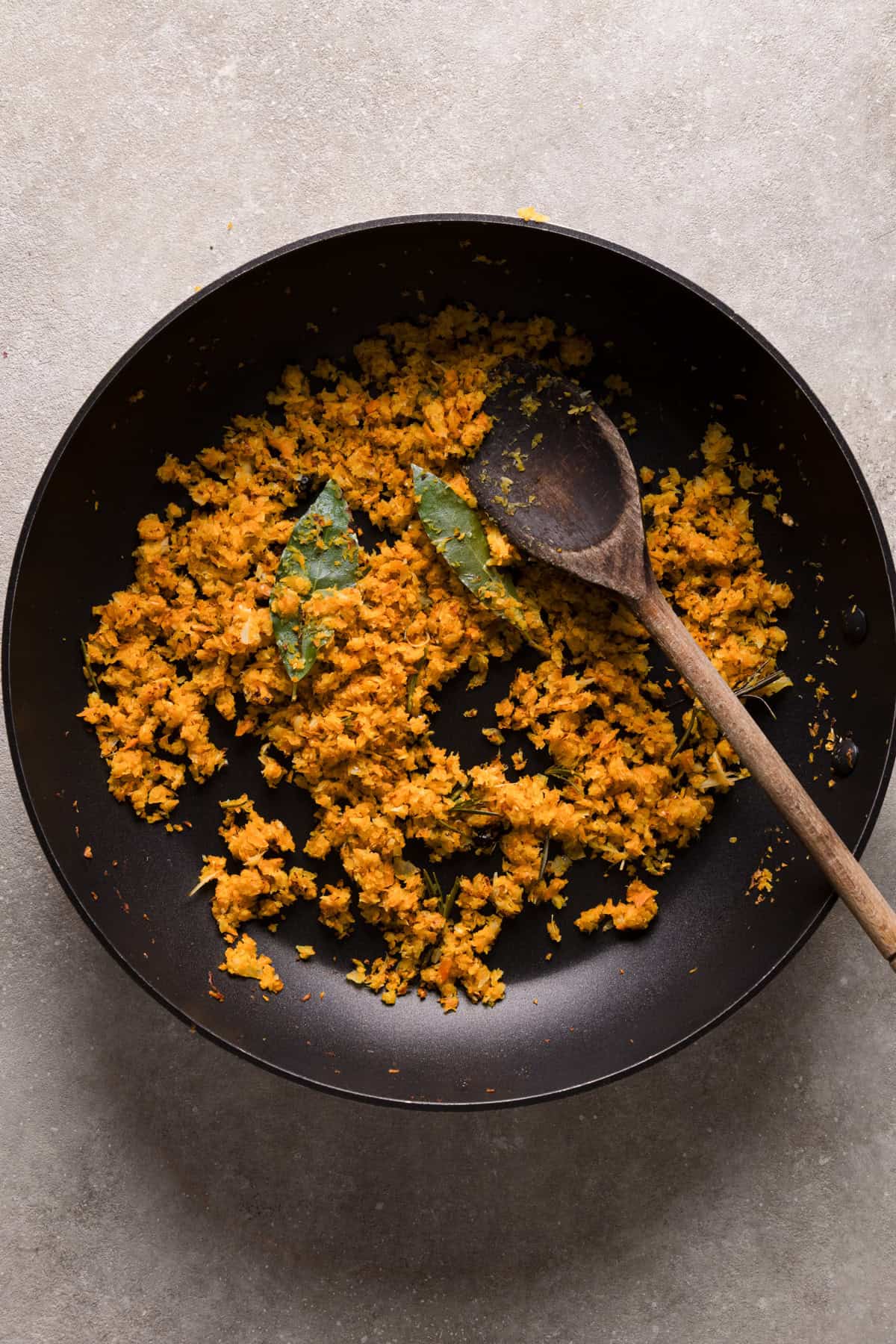 A frying pan with shredded veggies and herbs on a white backdrop.