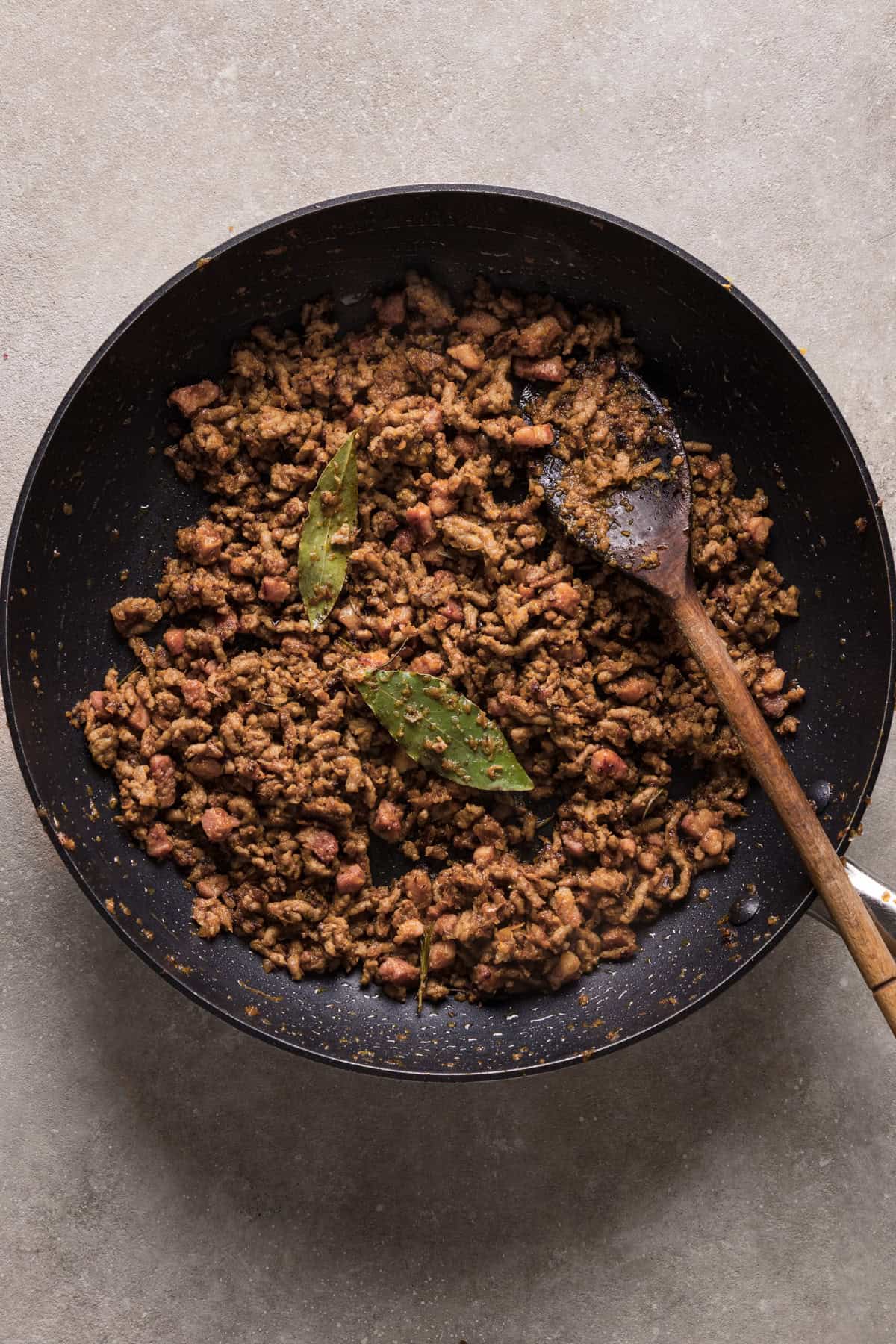 A frying pan with ground pork, and bay leaves on a white background.