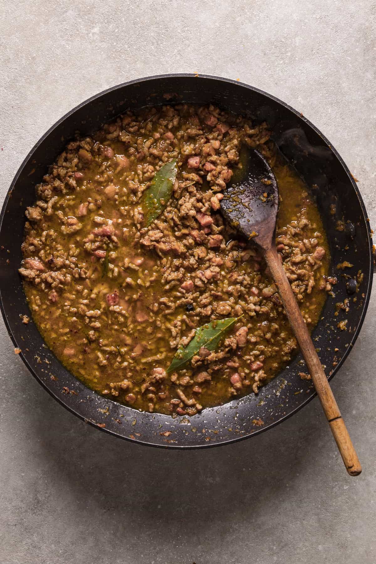 A frying pan with cooked meat and broth on a white background.
