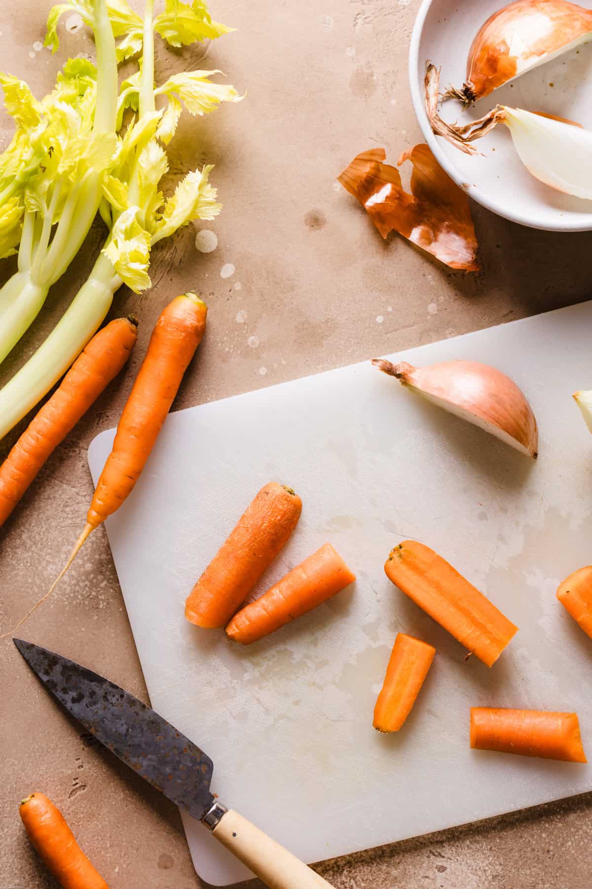 a photo showing the step process of hoe to cut the veggies. Some carrots cut into chunks on a chopping board next to the celery, onion and a knife
