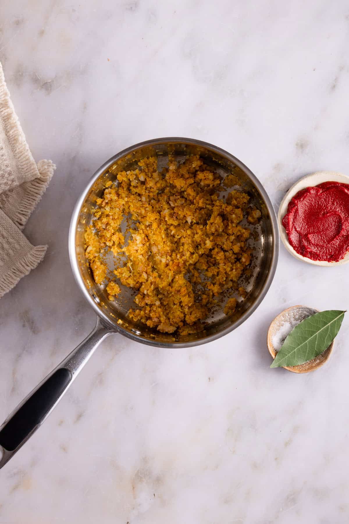 A large sauce pan with cooked carrots, celery, onions and pancetta. Next a pinch bowl with a bay leaf on top.