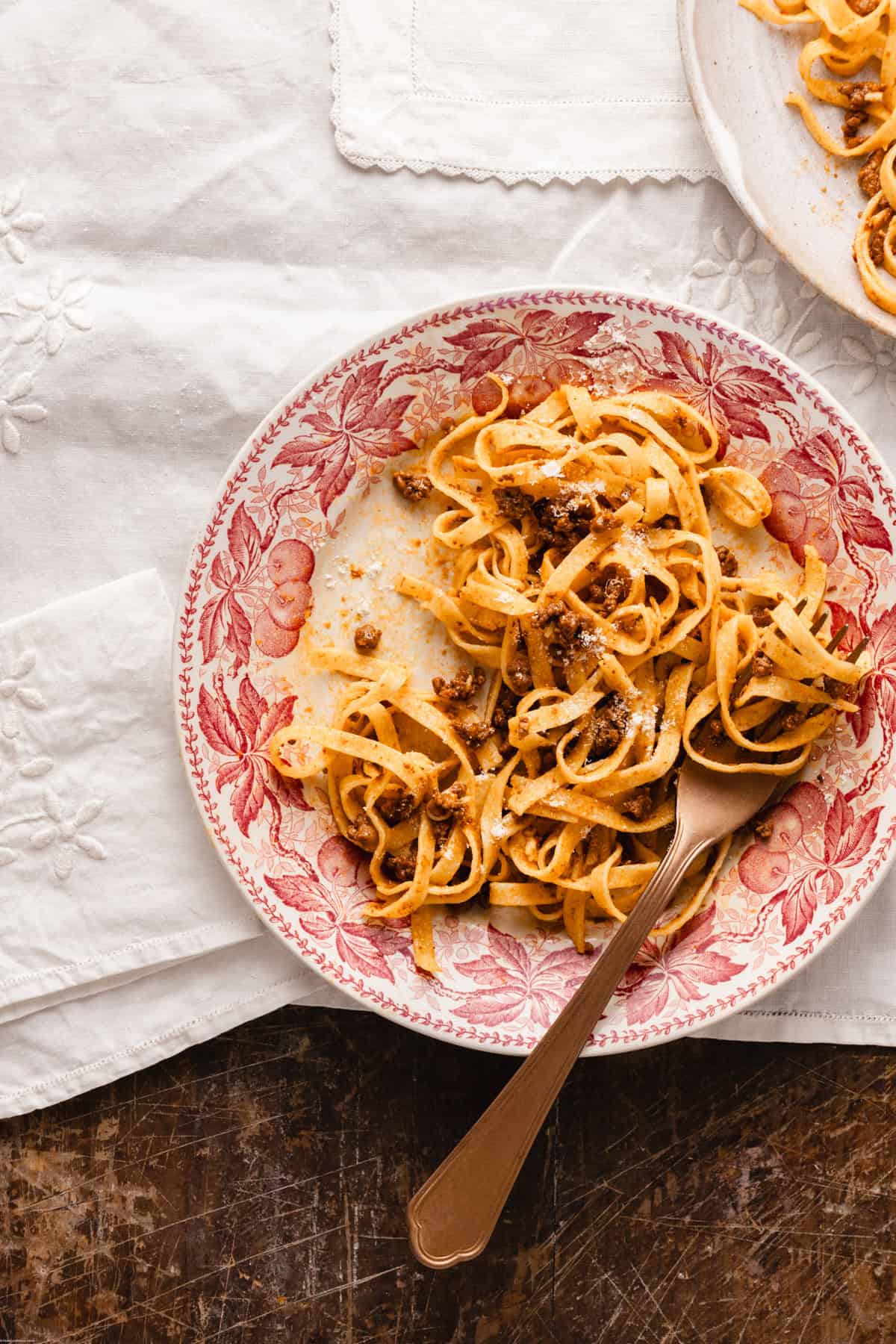 Tagliatelle al ragu placed on a pink vintage plate with a fork on top