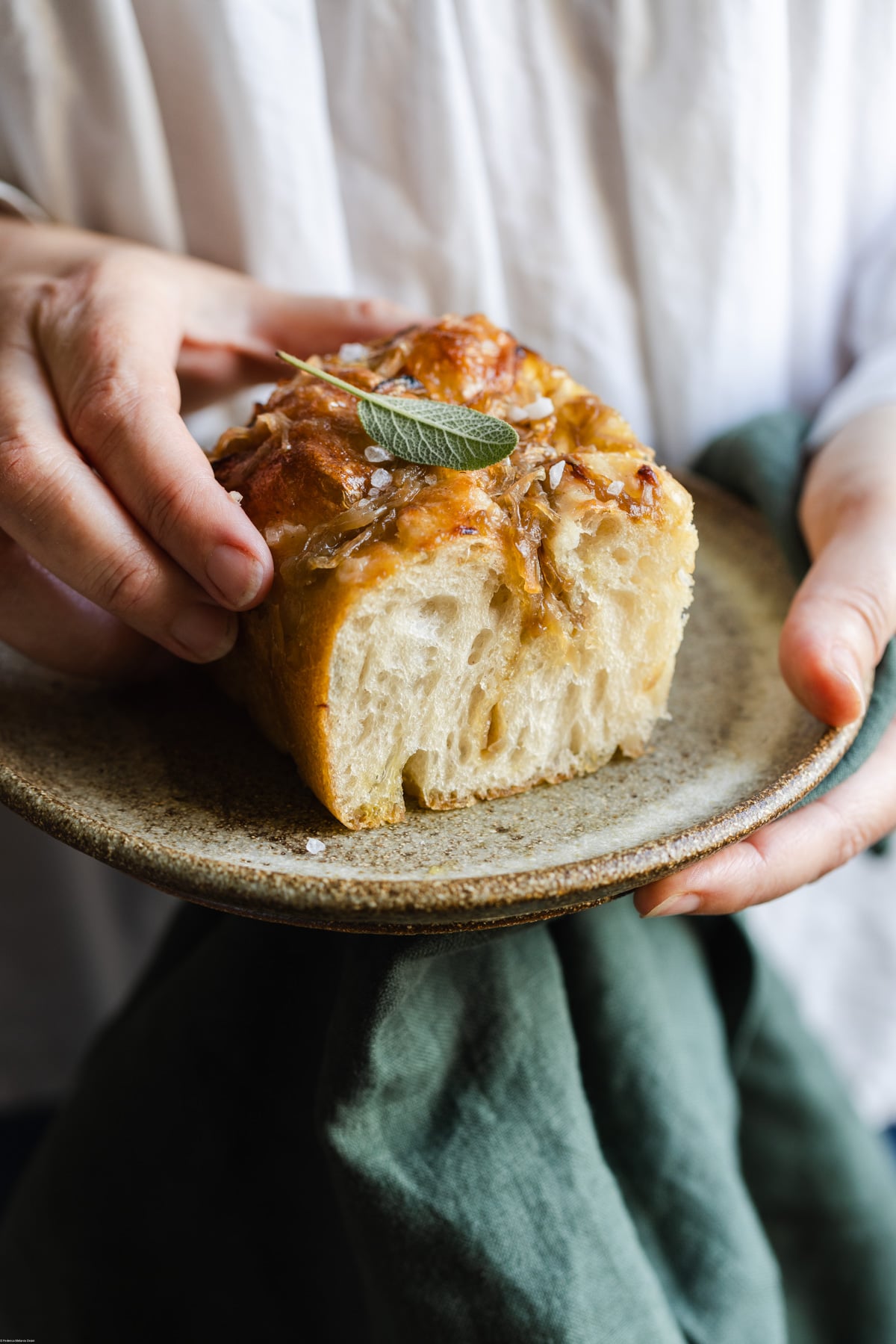 hand holding a slice of caramelized onion focaccia placed on top of a plate