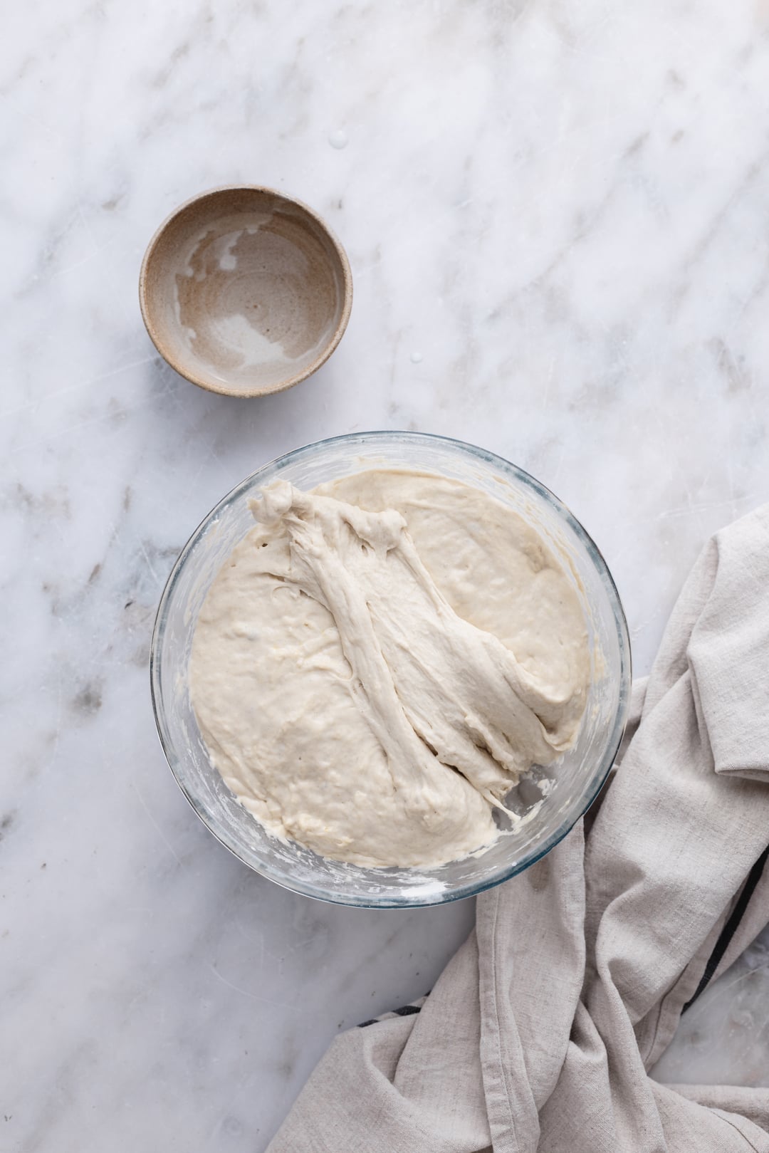 Showing the folding technique. One side of the focaccia dough fold it over the other side in a big bowl set on a marble surface.