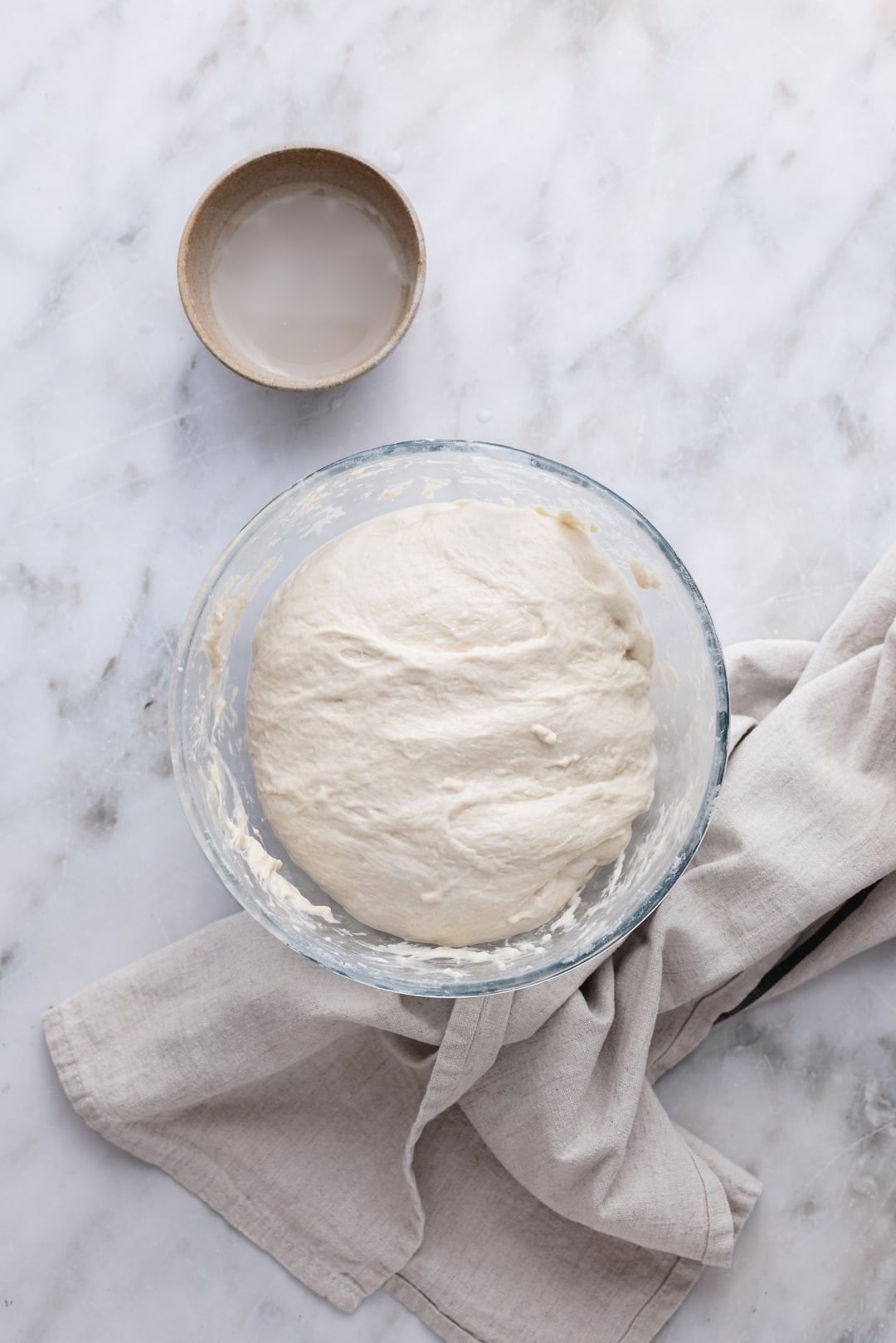 Focaccia dough folded on a big bowl set on a marble surface.