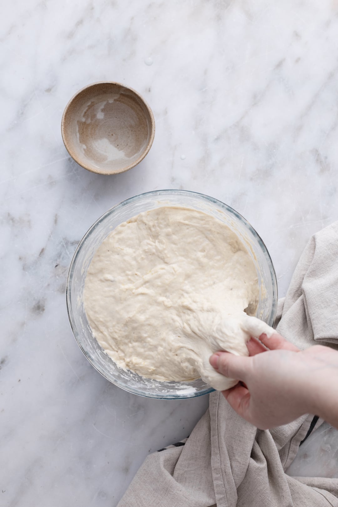 Hands stretching on side of the dough set on a marble surface.