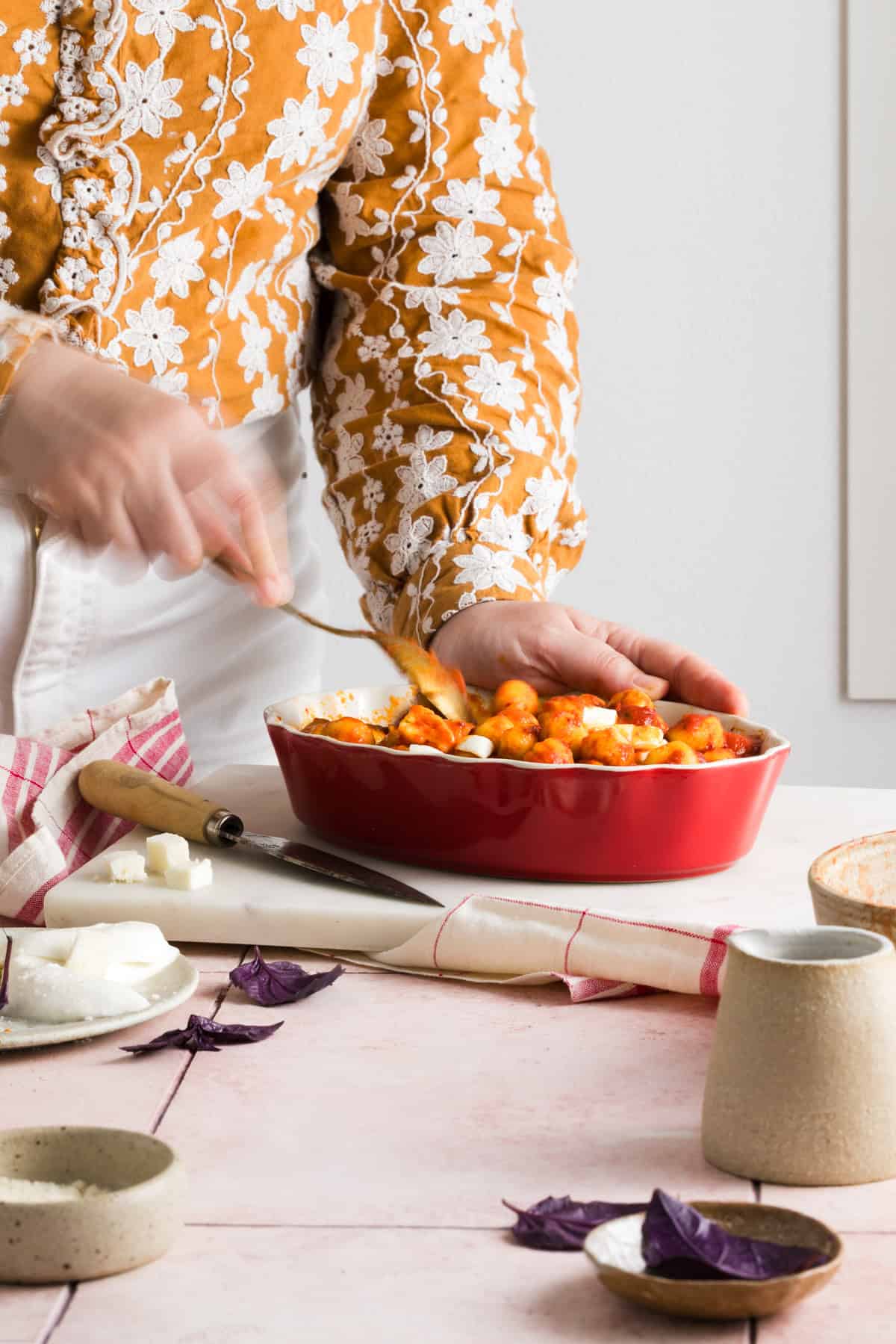 human mixing the gnocchi with a spoon on baking tray