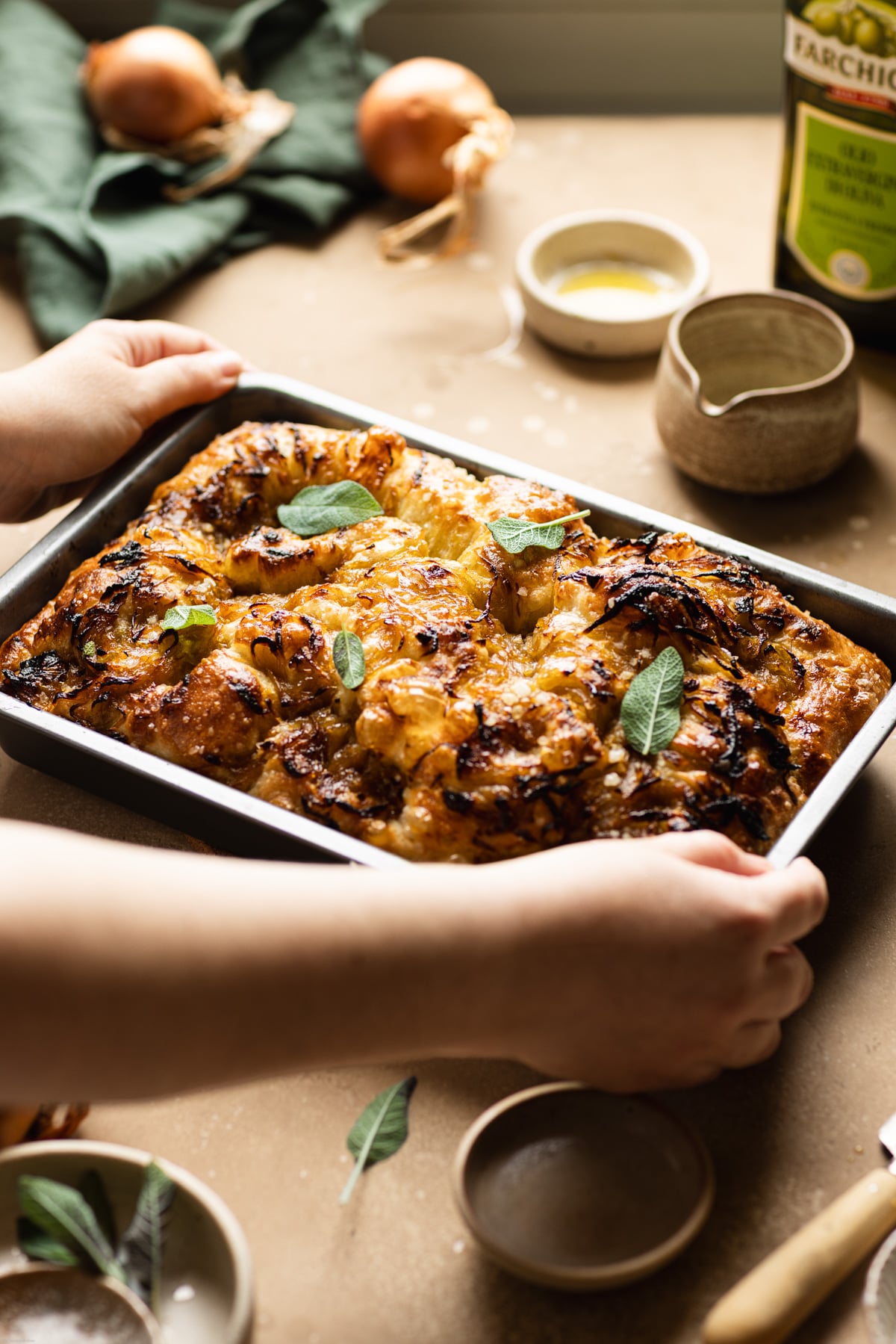 hand holding the focaccia topped with onions and sage leaves