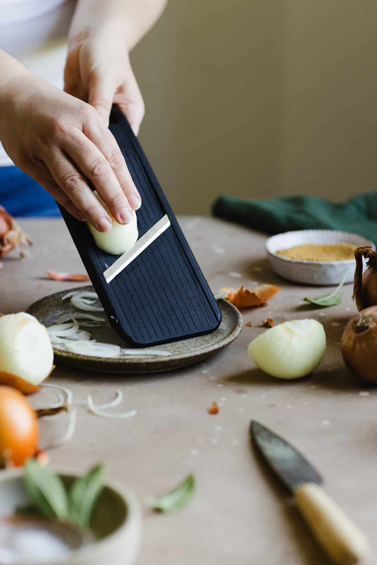 hand slicing the onion with a mandolin placed on a plate