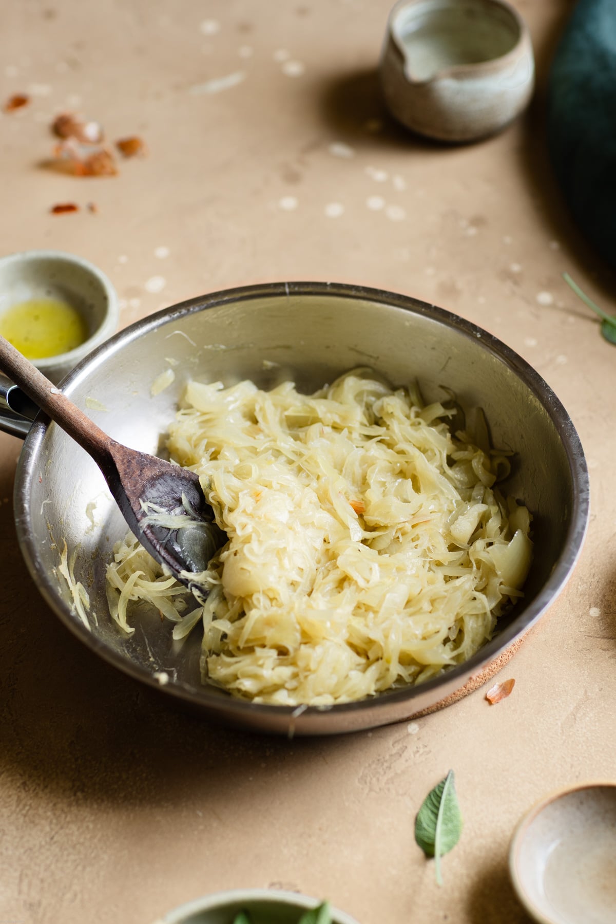 sautéed onion in a frying pan on a brown backdrop surrounded by olive oil, sage leaves, and green towel